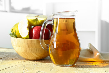 Jug of tasty apple juice and bowl with fruits on table