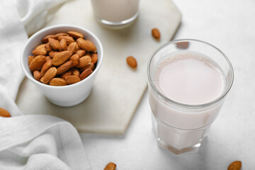 Glass of healthy almond milk and bowl with nuts on light background