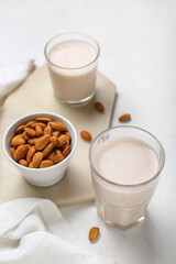 Board with glasses of healthy almond milk and nuts on light background