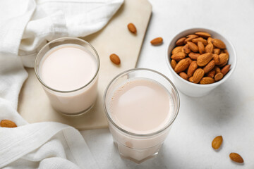 Board with glasses of healthy almond milk and nuts on light background