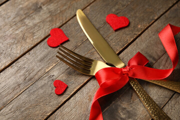 Golden cutlery for Valentine's Day with red bow and hearts on wooden background, closeup