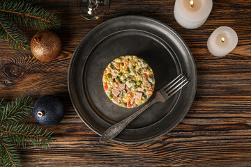 Plate of Olivier salad, Christmas branches, balls and candles on wooden table