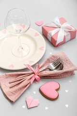Table setting for Valentine's Day with gift and pink hearts on grey background, closeup