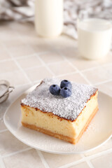 Plate with piece of cheese pie and blueberries on white table