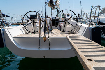 White sailing yacht on the quay in the port on a cloudy day, view from the stern. High-quality photo. boat stern with big steering wheel and sailboat stern deck. Close-up