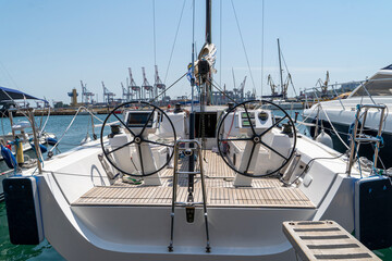 White sailing yacht on the quay in the port on a cloudy day, view from the stern. High-quality photo. boat stern with big steering wheel and sailboat stern deck. Close-up