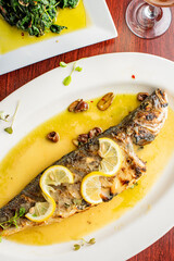 Grilled Fish. Branzino, whole grilled sea bream. Classic regional Greek  seafood favorite. Whole fish, grilled with skin in, served with lemon potatoes lemons Italian parsley and capers.