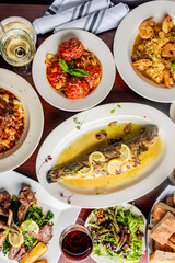 Grilled Fish. Italian Dinner table. Pasta, grilled sea bream. Classic regional Greek  seafood favorite. Whole fish, grilled with skin in, served with lemon potatoes lemons Italian parsley and capers.
