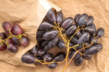One bunch of juicy organic black grapes with paper bag on craft paper, close-up, top view.