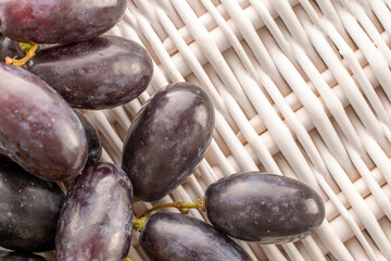 Several berries of juicy organic black grapes on a vine mat, close-up, top view.