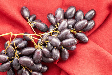 One bunch of juicy organic black grapes on a red linen napkin, close-up, top view.