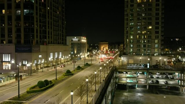 aerial footage of a long street with tall light posts along the sidewalk with bare winter trees at night and cars driving along the street surrounded by skyscrapers and office buildings in Atlanta