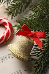Golden shiny bell with red bow and fir branches on music sheet, closeup. Christmas decoration