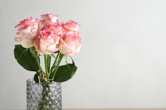 Vase with beautiful pink roses on light grey background, closeup. Space for text