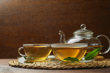 Fresh green tea in glass cups, leaves and teapot on wooden table