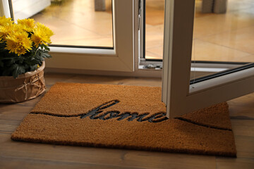 Doormat with word Home and flowers on parquet floor indoors