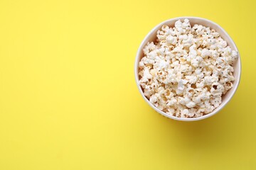 Paper bucket with delicious popcorn on yellow background, top view. Space for text