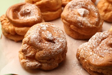Delicious profiteroles with powdered sugar on parchment paper, closeup