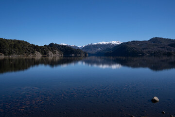 Fototapeta premium Alpine landscape in summer. Panorama view of the calm lake, forest and volcano Batea Mahuida, under a deep blue sky. Beautiful environment reflection in the water surface. 
