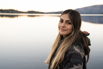 Portrait of a young woman smiling. The placid lake and mountain range in the background. Beautiful...
