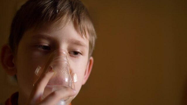 caucasian boy is treated by breathing in a mask with inhalations. treatment of allergy cough by inhalation. a boy at home breathes in a mask with an inhaler.copyspace on the right