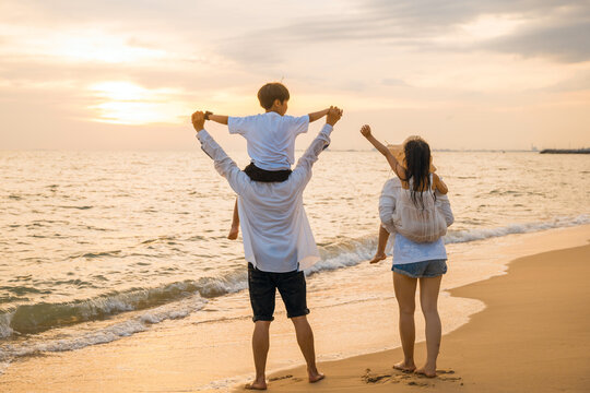 Happy family in holiday. Father, Mother and kids having fun together shoulder ride on summer beach, Parents carrying children on shoulders at beach on sunset time, Family on holiday summer vacation