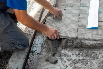 Bricklayer lays tiles on cement. Photo of hand with tile close-up. Authentic workflow. Construction background..