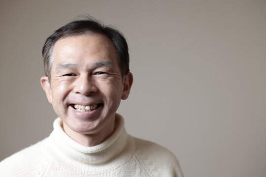 Middle-aged Asian Man In White Turtleneck Wool Sweater Under Gray Background. Concept Image Of Warm Biz, Stability In Daily Life, And Sustainable Living.