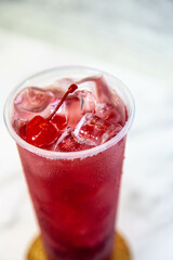 Lemonade with ice and red cherries in a large plastic glass