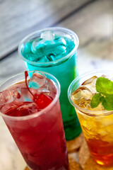 Three juicy lemonades of different colors in transparent plastic glasses with ice