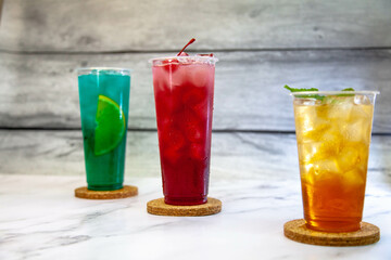 Three juicy lemonades of different colors in transparent plastic glasses with ice