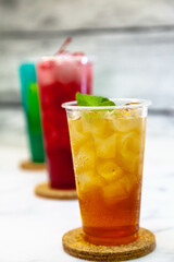 Three juicy lemonades of different colors in transparent plastic glasses with ice