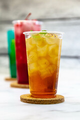 Three juicy lemonades of different colors in transparent plastic glasses with ice