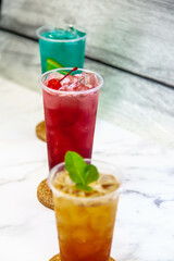 Three juicy lemonades of different colors in transparent plastic glasses with ice