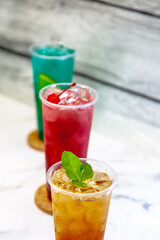 Three juicy lemonades of different colors in transparent plastic glasses with ice
