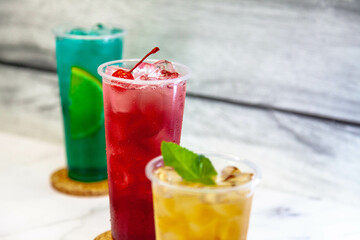 Three juicy lemonades of different colors in transparent plastic glasses with ice