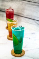 Three juicy lemonades of different colors in transparent plastic glasses with ice