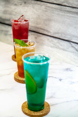 Three juicy lemonades of different colors in transparent plastic glasses with ice