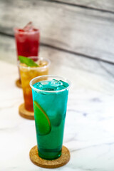 Three juicy lemonades of different colors in transparent plastic glasses with ice