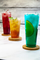 Three juicy lemonades of different colors in transparent plastic glasses with ice