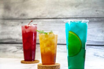 Three juicy lemonades of different colors in transparent plastic glasses with ice