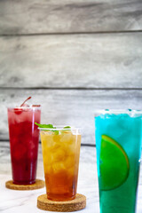 Three juicy lemonades of different colors in transparent plastic glasses with ice