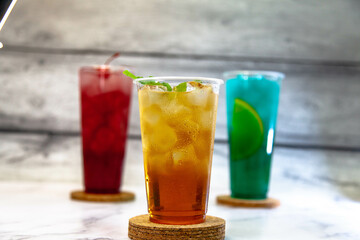 Three juicy lemonades of different colors in transparent plastic glasses with ice