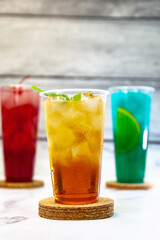 Three juicy lemonades of different colors in transparent plastic glasses with ice