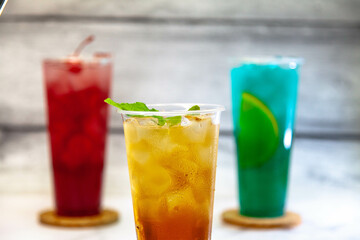 Three juicy lemonades of different colors in transparent plastic glasses with ice
