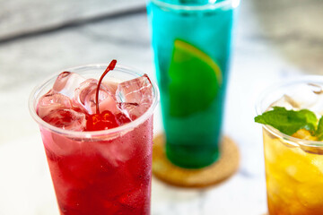 Three juicy lemonades of different colors in transparent plastic glasses with ice