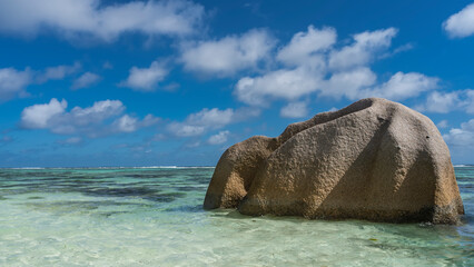 A huge granite boulder with folded slopes rises in the ocean. Clear turquoise water and blue sky...