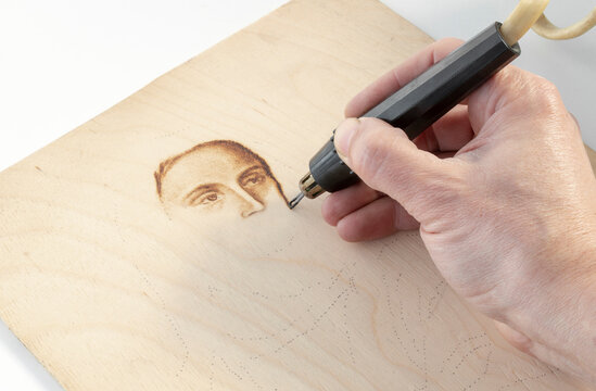 Close-up drawing a portrait using hand burning wood with a pyrography pen, handmade, hobby