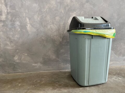 Gray trash can with the lid in front of concrete background.