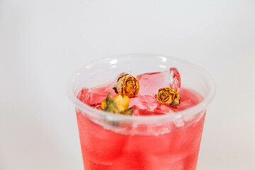 Red lemonade with ice and yellow rose buds on a white background.